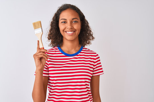 Young brazilian painter woman holding brush standing over isolated white background with a happy face standing and smiling with a confident smile showing teeth