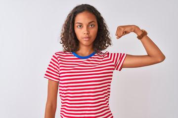Obraz na płótnie Canvas Young brazilian woman wearing red striped t-shirt standing over isolated white background Strong person showing arm muscle, confident and proud of power