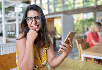 Candid lifestyle portrait of laughing hispanic millennial student typing on cellphone in modern...