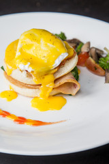 Eggs Benedict -American breakfast or brunch dish that consists of two halves of an English muffin topped with a poached egg, bacon or ham, and hollandaise sauce. 