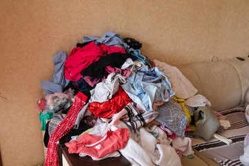 Front view of colorful childish clothes scattered on sofa at home. Big bunch of clothes lying at...
