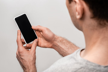 cropped view of young man holding smartphone with blank screen isolated on grey