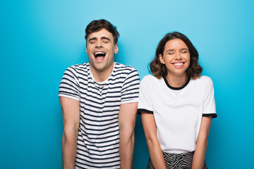 excited man and woman laughing with closed eyes on blue background