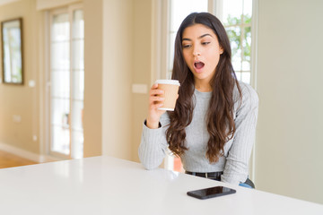 Young woman drinking a cup of coffee at home scared in shock with a surprise face, afraid and excited with fear expression