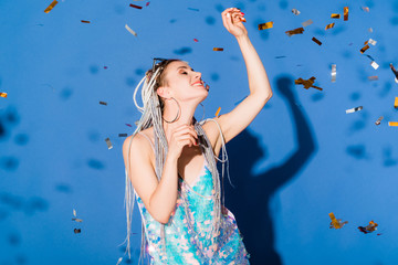 Obraz na płótnie Canvas beautiful smiling stylish girl Gesturing on blue with confetti