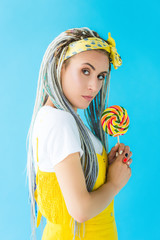girl with dreadlocks holding lollipop and looking at camera isolated on turquoise