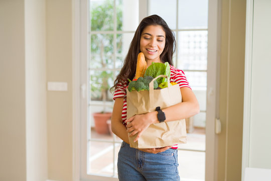 Beautiful young woman smiling holding a paper bag full of fresh groceries at home