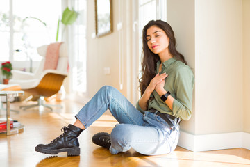 Young beautiful woman sitting on the floor at home smiling with hands on chest with closed eyes and grateful gesture on face. Health concept.