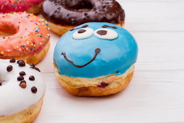 Blue funny donut on wooden table. Glazed decorated donuts for sweet break on white wooden background. Flat lay, copy space.