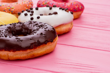 Tasty donuts on pink wooden background. Cakes with colorful frosting. Space for text.