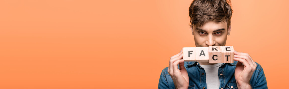 panoramic shot of positive man showing wooden cubes with fake fack lettering isolated on yellow