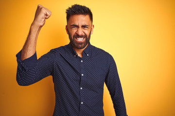 Young handsome indian businessman wearing shirt over isolated yellow background angry and mad raising fist frustrated and furious while shouting with anger. Rage and aggressive concept.