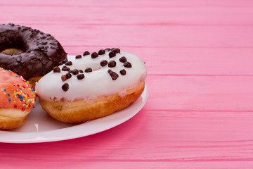 Plate with donuts on pink wooden background. Cakes with icing, copy space. Sweet yummy dessert.