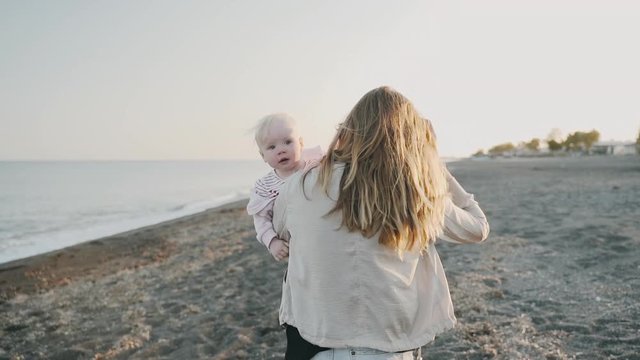 A young woman walks along the sea coast with her yearling daughter