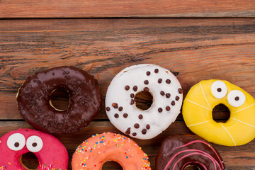 Variety of donuts on wooden table. Colored iced donuts on brown wood background.
