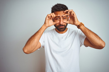 Young indian man wearing t-shirt standing over isolated white background Trying to open eyes with fingers, sleepy and tired for morning fatigue