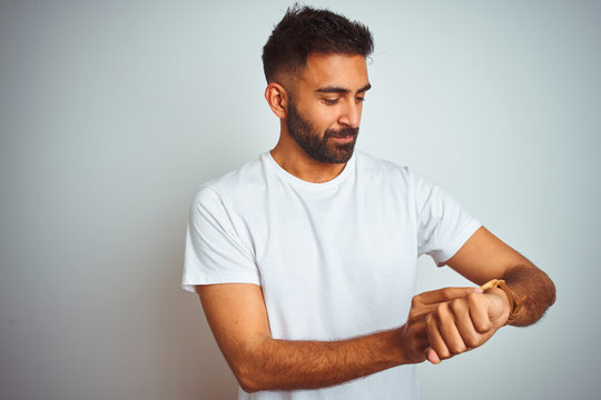 Young indian man wearing t-shirt standing over isolated white background Checking the time on wrist watch, relaxed and confident