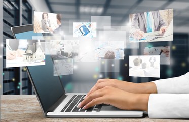 Male hand holding smartphone while sitting at table near laptop with digital holograms