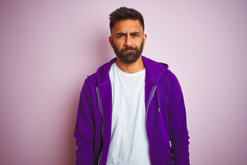 Young indian man wearing purple sweatshirt standing over isolated pink background skeptic and nervous, frowning upset because of problem. Negative person.