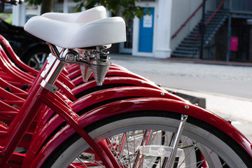 Fototapeta premium Red Bicycles For Rent With White Seat and White Wheels In A Row In A Rack In A Parking Lot