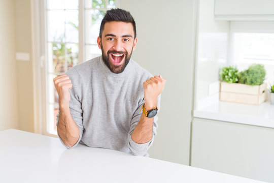 Handsome hispanic man wearing casual sweater at home celebrating surprised and amazed for success with arms raised and open eyes. Winner concept.