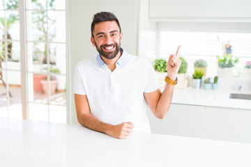 Handsome hispanic man casual white t-shirt at home with a big smile on face, pointing with hand and finger to the side looking at the camera.