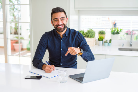 Handsome hispanic man working using computer and writing on a paper very happy pointing with hand and finger
