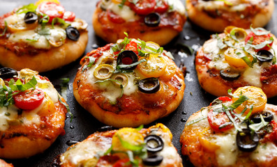 Mini pizzas with the addition of cherry tomatoes, olives, mozzarella cheese and fresh basil on a...