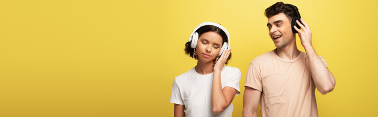 panoramic shot of young man and woman listening music in headphones on yellow background