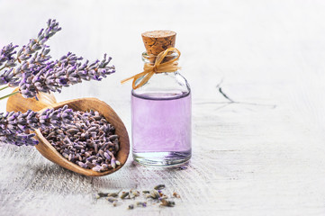 Glass bottle of Lavender essential oil with fresh lavender flowers and dried lavender seeds on white wooden rustic table, aromatherapy spa massage concept. Lavendula oleum