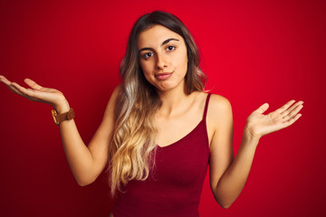 Young beautiful woman wearing a t-shirt over red isolated background clueless and confused...