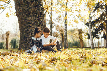 little beautiful dark-skinned girl sitting in the autumn park with her European little friend