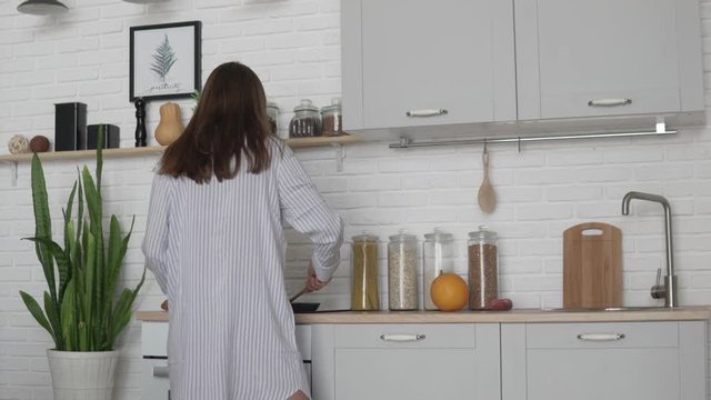 Young woman in nightie prepares breakfast in the kitchen in the morning. a cheerful man comes to her and kisses her