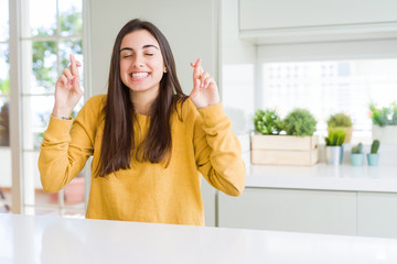 Beautiful young woman wearing yellow sweater smiling crossing fingers with hope and eyes closed. Luck and superstitious concept.