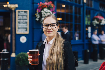 Young business lady in glasses standing by the pub with a pint of the beer.