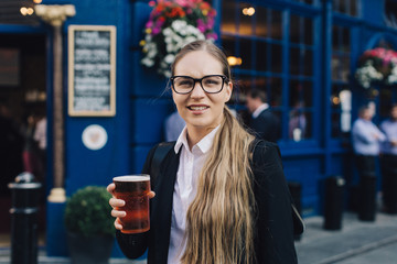 Young business lady in glasses standing by the pub with a pint of the beer.