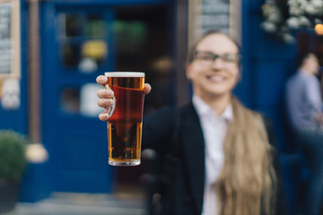 Young business lady in glasses standing by the pub with a pint of the beer.