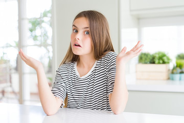 Beautiful young girl kid wearing stripes t-shirt clueless and confused expression with arms and...