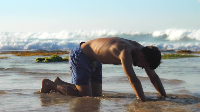 handsome man does yoga exercises near endless ocean under blue sky in sumer extreme slow motion. Concept spiritual practices and healthy lifestyle
