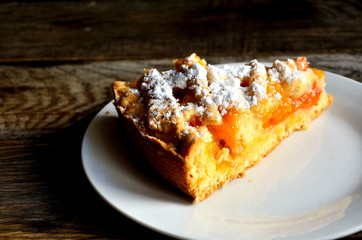 Slice of homemade apricot pie in a white plate on a wooden table.