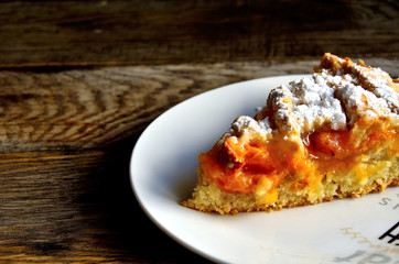 Slice of homemade apricot pie in a white plate on a wooden table.