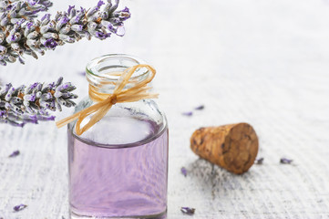 Fototapeta na wymiar Glass bottle of Lavender essential oil with fresh lavender flowers and dried lavender seeds on white wooden rustic table, aromatherapy spa massage concept. Lavendula oleum