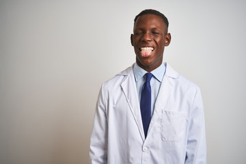 Young african american doctor man wearing coat standing over isolated white background sticking tongue out happy with funny expression. Emotion concept.