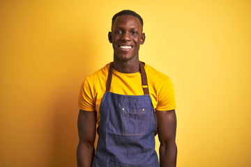African american bartender man wearing apron standing over isolated yellow background with a happy and cool smile on face. Lucky person.