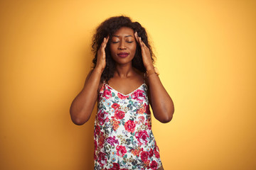 African american woman wearing floral summer t-shirt over isolated yellow background with hand on head for pain in head because stress. Suffering migraine.