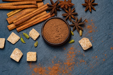 Fototapeta na wymiar Brown star anise and cinnamon on a dark background. Ground cinnamon in a cup. Cardamom and cane sugar.
