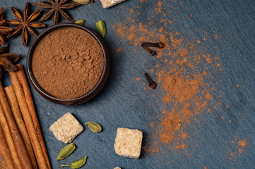 Brown star anise and cinnamon on a dark background. Ground cinnamon in a cup. Cardamom and cane sugar.