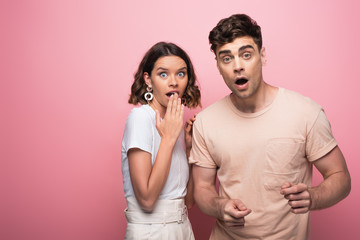 young, scared man and woman gesturing and looking at camera on pink background