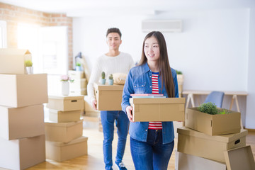 Beautiful young asian couple looking happy holding cardboard boxes, smiling excited moving to a new home