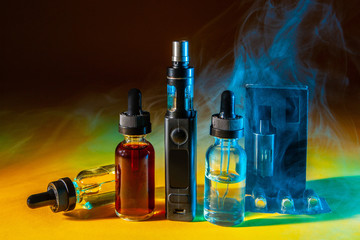 The vaping concept. E-cigs. Vaping set in a multicolored smoke. Vapes and bottles with filling liquid. Electronic devices for smoking. Modern smoking gadgets.